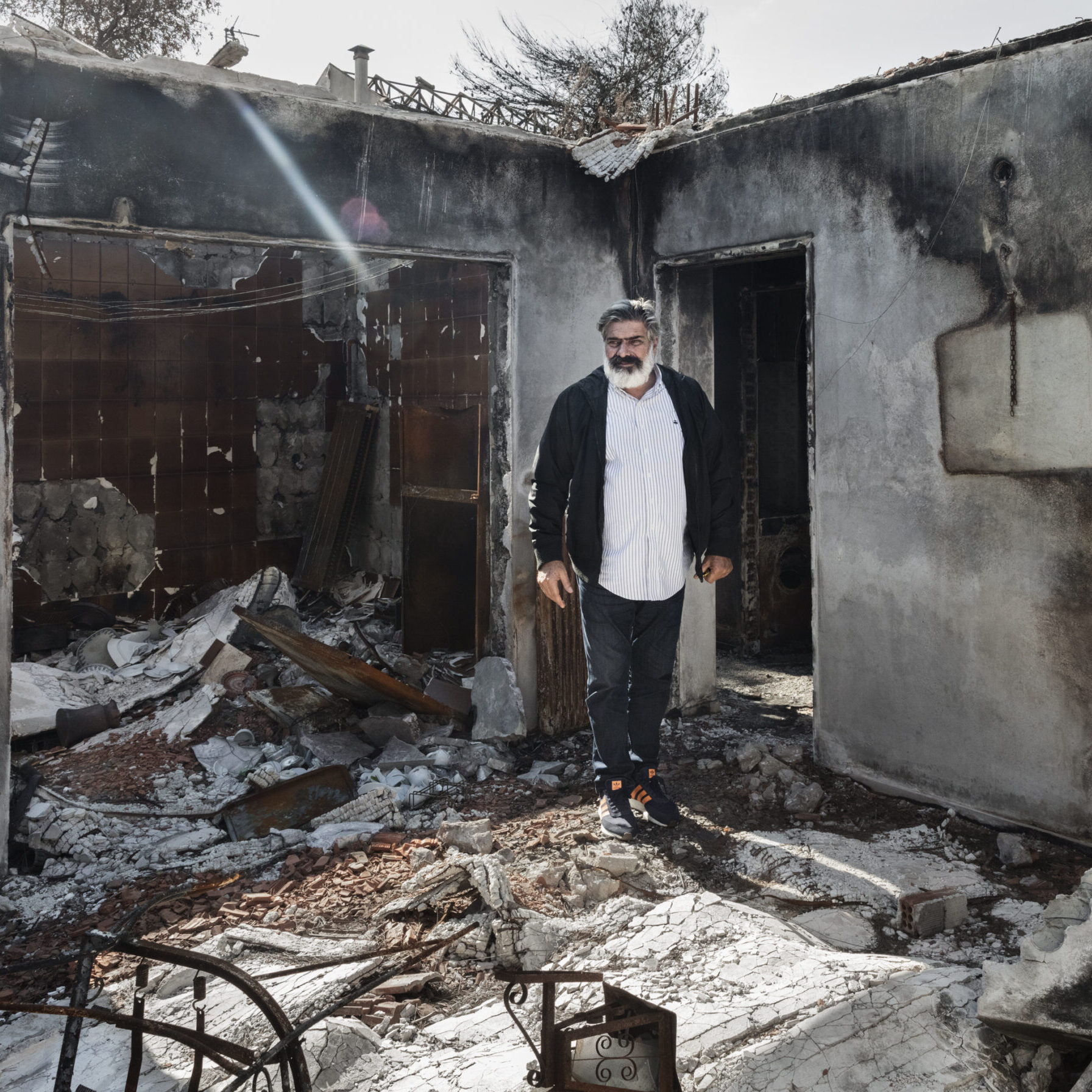 A man standing in the ruins of his house after a forest fire has swept through.
